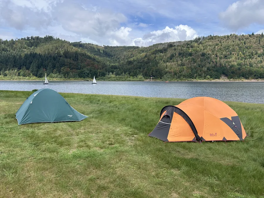 Blick über die Talsperre mit Bergen im Hintergrund, im Vordergrund eine Fahne am Steg